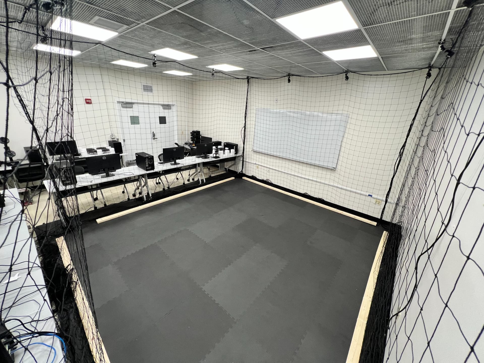 AVRC indoor flight area with safety netting, floor mats, and ground-station workstations